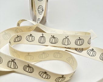 May include: A roll of off-white cotton ribbon with a black pumpkin print. The ribbon is rolled up and there are several loops of ribbon on a white surface.