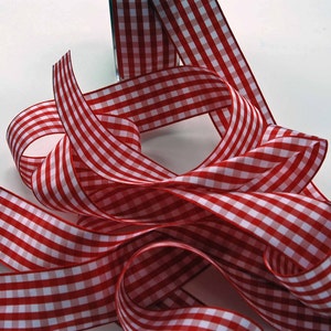 May include: A length of red and white gingham ribbon, with its distinctive checked pattern, is shown in a series of loops. The ribbon is neatly folded, and the fabric has a slight sheen. This ribbon is suitable for crafts and gift wrapping.
