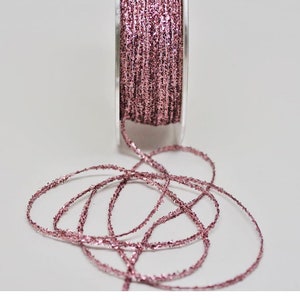 Puede incluir: Una bobina de hilo de purpurina rosa. El hilo está enrollado alrededor de una bobina de plástico transparente y está listo para ser utilizado para manualidades o decoración.