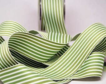 May include: Green and white striped ribbon, unspooled and curled, with a roll of ribbon in the background. The ribbon has a repeating pattern of vertical stripes in shades of green and white. The ribbon is likely used for crafting or gift wrapping.