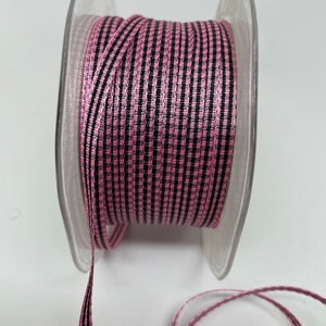 May include: A spool of pink and black striped ribbon. The ribbon is on a clear plastic spool.