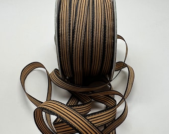 May include: A spool of black and tan striped ribbon. The ribbon is wound around a silver spool.