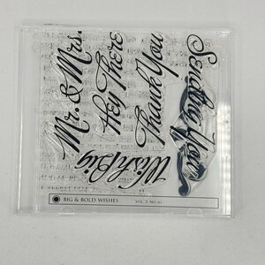 May include: A clear plastic sheet with six rubber stamps. The stamps feature the phrases "Mr. & Mrs.", "Hey There", "Thank You", "Wish Big", "Sending You" and "Big & Bold Wishes Vol. 3 No. 01".