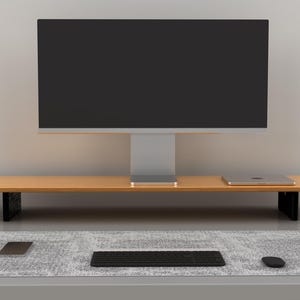 May include: A modern desk setup featuring a large monitor, wooden shelf, laptop, keyboard, mouse, and two gray speakers. The desk is set on a gray surface with a gray rug. The monitor is black.