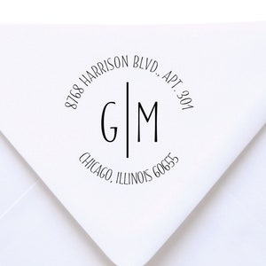May include: A stack of white envelopes with a custom address stamp. The stamp is circular with the initials "G" and "M" separated by a vertical line. The address includes "8768 Harrison Blvd., Apt. 301, Chicago, Illinois 60655."