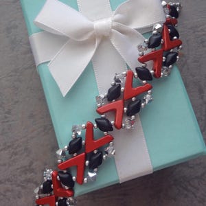 May include: A beaded bracelet featuring a repeating pattern of matte black diamond-shaped beads, glossy red chevron-shaped beads, and small clear faceted crystal beads, all connected with tiny silver-colored metallic spacer beads.