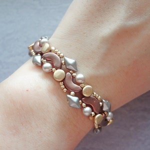 May include: A bracelet made with silver, gold, and copper coloured beads. The beads are arranged in a pattern of crescents, squares, and circles.