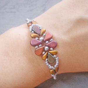 May include: A beaded bracelet featuring a central floral-inspired pattern made of teardrop-shaped beads in metallic shades of copper, bronze, and plum, accented by small silver seed beads arranged in a delicate, woven, and symmetrical design.