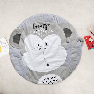 May include: A grey and white monkey play mat with the name "George" written on it. The mat is round and has a soft, plush texture.