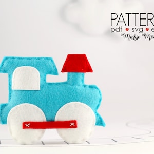 May include: A felt toy train with a blue engine, white wheels, and a red chimney. The train is on a white surface with a gray line.