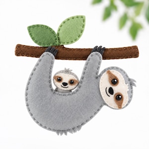 May include: A felt sloth ornament featuring a large grey adult sloth and a smaller baby sloth clinging to its chest. Both sloths have cream-colored faces with dark brown eye patches and black eyes. They hang from a brown felt branch with two green leaves.