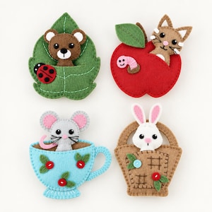 May include: Four felt appliques featuring a brown bear on a green leaf with a ladybug, a tan cat in a red apple with a pink worm, a gray mouse in a light blue teacup with red berries, and a white rabbit in a tan woven basket with green leaves.