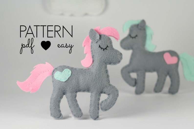 May include: Two gray felt toy horses with pink and teal accents. The horse on the left has a pink mane and tail, and a teal heart on its side. The horse on the right has a teal mane and tail, and a pink heart on its side. The text "PATTERN pdf &hearts; easy" is visible in the top left corner of the image.