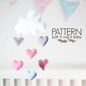 Puede incluir: Una nube de fieltro blanco con seis corazones de fieltro colgando de ella. Los corazones son en tonos de rosa y azul. El texto "PATTERN pdf ♥ svg ♥ easy  ♥ Maisie ♥ Moo" está impreso debajo de la nube.