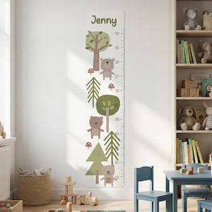 Può includere: Un adesivo da parete verticale per misurare l'altezza con il nome Jenny in alto. Il design include illustrazioni di orsi marroni, alberi verdi e piccoli funghi rossi. Una scala di misurazione nera è stampata sul lato destro in centimetri.