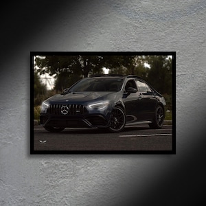 May include: A framed photograph of a dark blue luxury sedan. The car is parked on a paved surface with trees in the background. The car has black rims and a black grill. The headlights are on, and the car appears to be in motion.