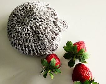 May include: A gray crocheted bowl with three red strawberries on a white surface.