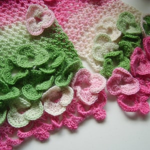 May include: A crocheted scarf with a gradient of pink, green and white. The scarf is decorated with crocheted flowers.