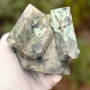 May include: A carved stone sculpture featuring a geometric, multi-faceted design with sharp, angular edges. The mineral displays a marbled texture with a colour palette of pale green, grey, and dark charcoal veins throughout the polished surface.