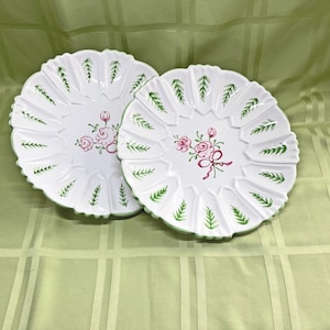 May include: Two white ceramic plates with green and pink floral designs. The plates have a scalloped edge and are decorated with green leaves and pink roses.