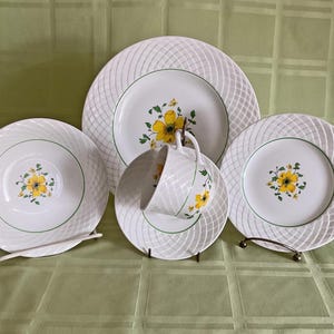 May include: A set of white ceramic dinnerware with a woven pattern and yellow floral design. The set includes a dinner plate, a salad plate, and a saucer.