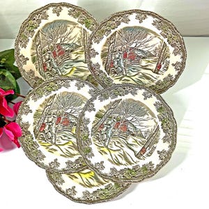 May include: A set of five vintage ceramic plates. Each plate features a winter scene with a red barn, trees, and a stone wall. The plates have a scalloped edge with a decorative border of leaves and vines.