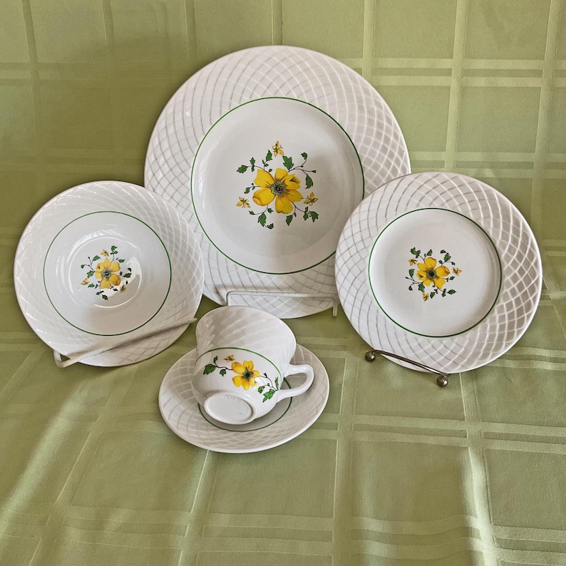 May include: A set of white ceramic dinnerware with a green and yellow floral design. The set includes a dinner plate, a salad plate, a saucer, and a teacup.