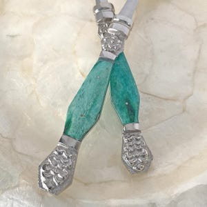 May include: Two crossed silver butter knives with turquoise handles. The handles have a marbled effect and are accented with silver bands. The ends of the knives have a decorative, textured design.