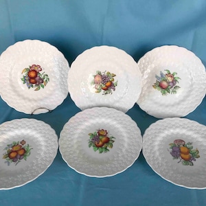 May include: Set of six white ceramic dinner plates with a raised, textured surface. Each plate features a colorful fruit design in the center.