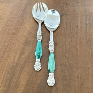 May include: A silver salad serving set, comprising a fork and spoon. The handles are turquoise with decorative silver detailing. The set is presented on a wooden surface.