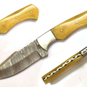 Può includere: Coltello fatto a mano con lama in acciaio Damasco e manico in osso giallo chiaro. L'impugnatura è fissata con tre piccoli rivetti. La lama ha un motivo unico e il coltello ha una ghiera argentata.