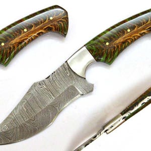 Puede incluir: Cuchillo de caza de acero de Damasco con una hoja curva y un mango con resina verde y marrón con pasadores de latón. El cuchillo tiene una virola plateada y una pieza de mango a juego.