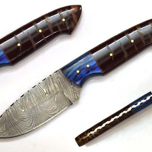 Può includere: Coltello in acciaio Damasco con manico marrone scuro, accentuato da dettagli blu e oro. La lama presenta un motivo ondulato unico. Il coltello è mostrato con due pezzi di manico aggiuntivi.