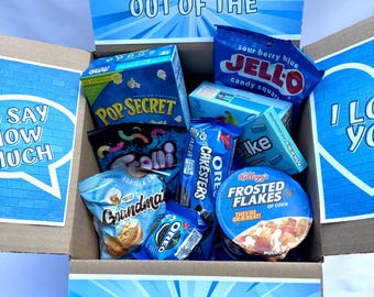 May include: A gift box filled with blue-themed snacks and treats. The box contains Pop Secret popcorn, Jell-O candy squares, Oreo cookies, and Kellogg's Frosted Flakes. The box has the words "SOMETHING OUT OF THE BLUE" and "BLUE" printed on it.