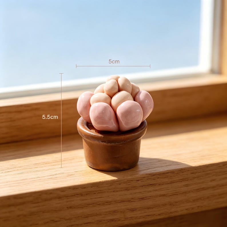 May include: A small, rounded succulent-shaped sculpture in a brown pot, featuring smooth, glossy, pale pink and beige bulbous segments. The object is marked with dimensions of 5cm in width and 5.5cm in height, indicating its compact size.