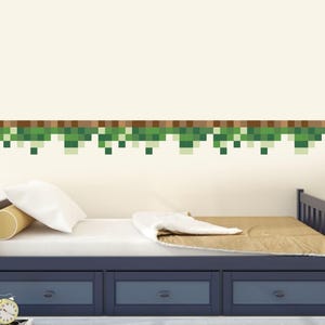 Könnte beinhalten: Ein pixeliger grün-brauner Rand verziert eine Schlafzimmerwand über einem marineblauen Bett mit drei Schubladen. Das Bett ist mit einem weißen Kissen, einem gelben Nackenkissen und einer braunen Decke ausgestattet. Ein Fußball und ein Wecker sind sichtbar.