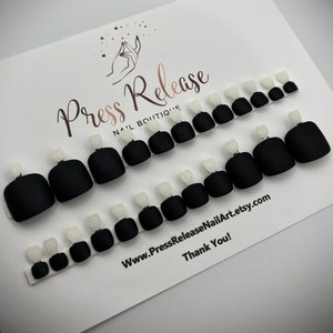 May include: Black matte press-on toenails with a white accent on each nail. The nails are arranged in rows on a white card with the text "Press Release Nail Boutique" and "www.PressReleaseNailArt.etsy.com Thank You!"