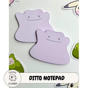 May include: Two lavender Ditto-shaped notepads with smiling faces are displayed on a white surface, surrounded by colorful character stickers. The text "Ditto Notepad" is below the notepads.