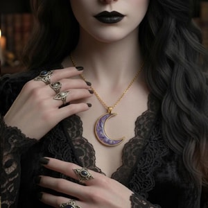 May include: A gold-toned necklace with a purple crescent moon pendant, accented with white stars, hangs against a black lace top. Several silver rings with dark stones adorn the fingers. The overall aesthetic is gothic and elegant.