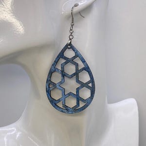 May include: Blue teardrop-shaped earrings with a geometric cutout design. The earrings are made of wood and have a silver hook.