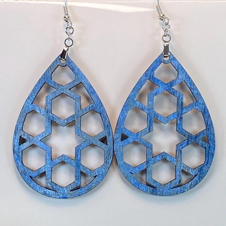 May include: A pair of blue teardrop-shaped earrings with a geometric pattern. The earrings are made of wood and have silver hooks.