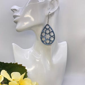 May include: A pair of teardrop-shaped earrings with a geometric cutout design. The earrings are made of blue and silver metal and have a silver hook closure.
