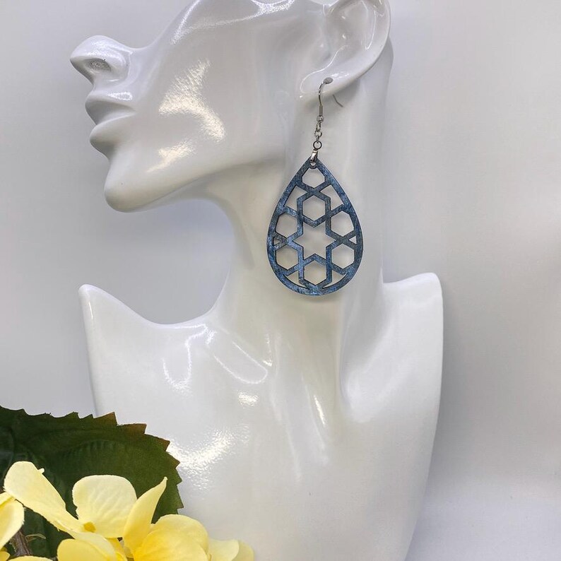 May include: A pair of teardrop-shaped earrings with a geometric cutout design. The earrings are made of blue and silver metal and have a silver hook closure.