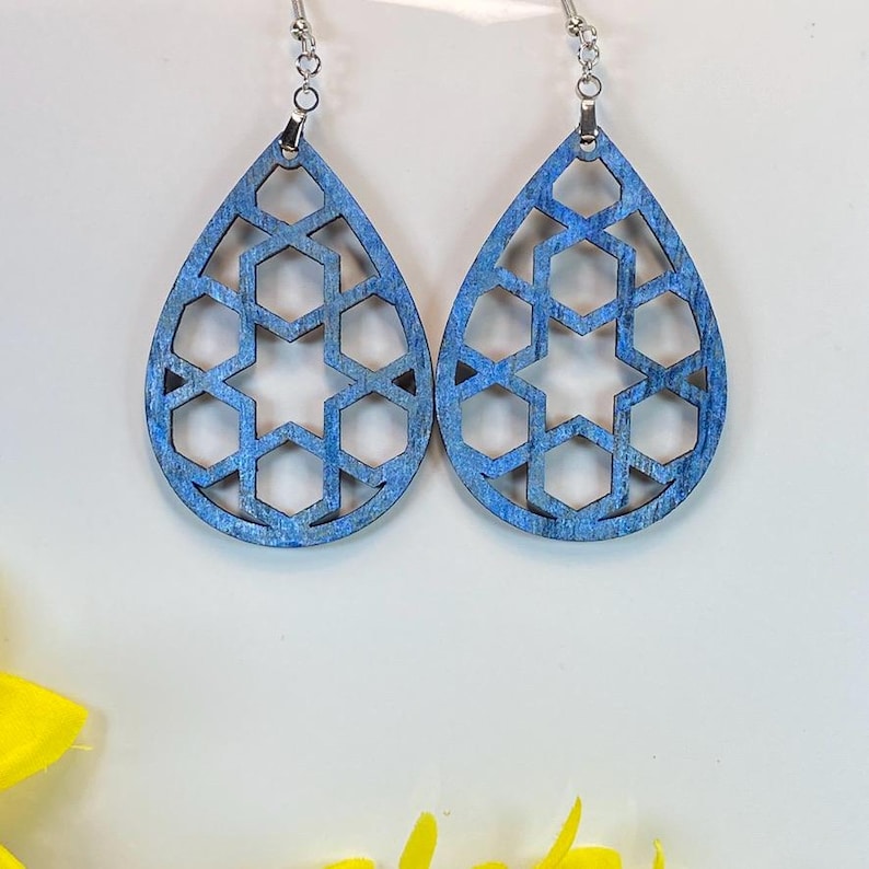 May include: A pair of blue teardrop-shaped earrings with a geometric design. The earrings are made of wood and have a silver hook.