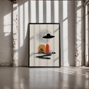 Puede incluir: Impresión artística abstracta enmarcada. La obra presenta un OVNI negro sobre un paisaje naranja y rojo, con un camino negro y un fondo gris arremolinado. La impresión está sobre un fondo crema, dentro de un marco negro.