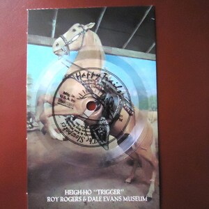 May include: A clear circular vinyl record featuring a printed image of a palomino horse rearing up. The record includes the text Happy Trails, The Slowpokes, and the Roy Rogers & Dale Evans Museum. The bottom text reads HEIGH-HO TRIGGER.