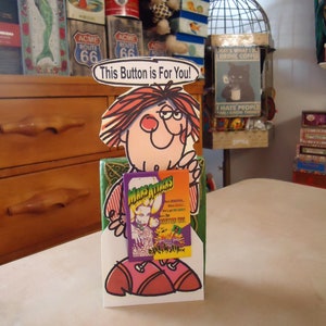 May include: A die-cut cardboard display stand featuring a cartoon character with brown hair and pink cheeks, holding a rectangular Mars Attacks trading card. Above the character, a speech bubble contains the text, This Button is For You!
