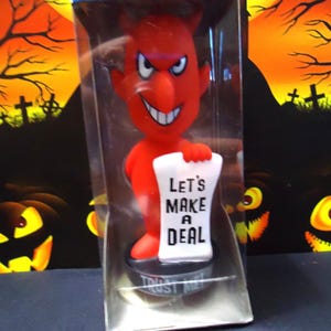 May include: A red devil figurine with horns, a wide grin, and the text "Let's Make a Deal" on a scroll. The figurine is packaged in a clear plastic box with the words "Wacky WiseCracks" on top. Halloween theme.