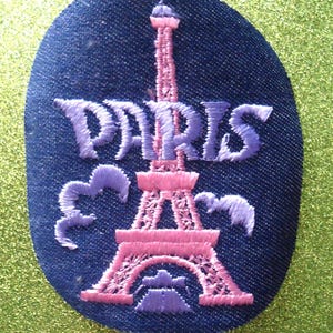 May include: A blue fabric patch with a pink embroidered Eiffel Tower and the word "PARIS" in purple embroidery.