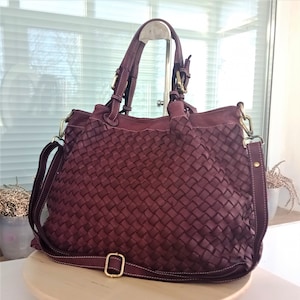 Pu&ograve; includere: Una grande borsa tote in pelle bordeaux con un design intrecciato. La borsa ha una lunga tracolla e due manici superiori.
